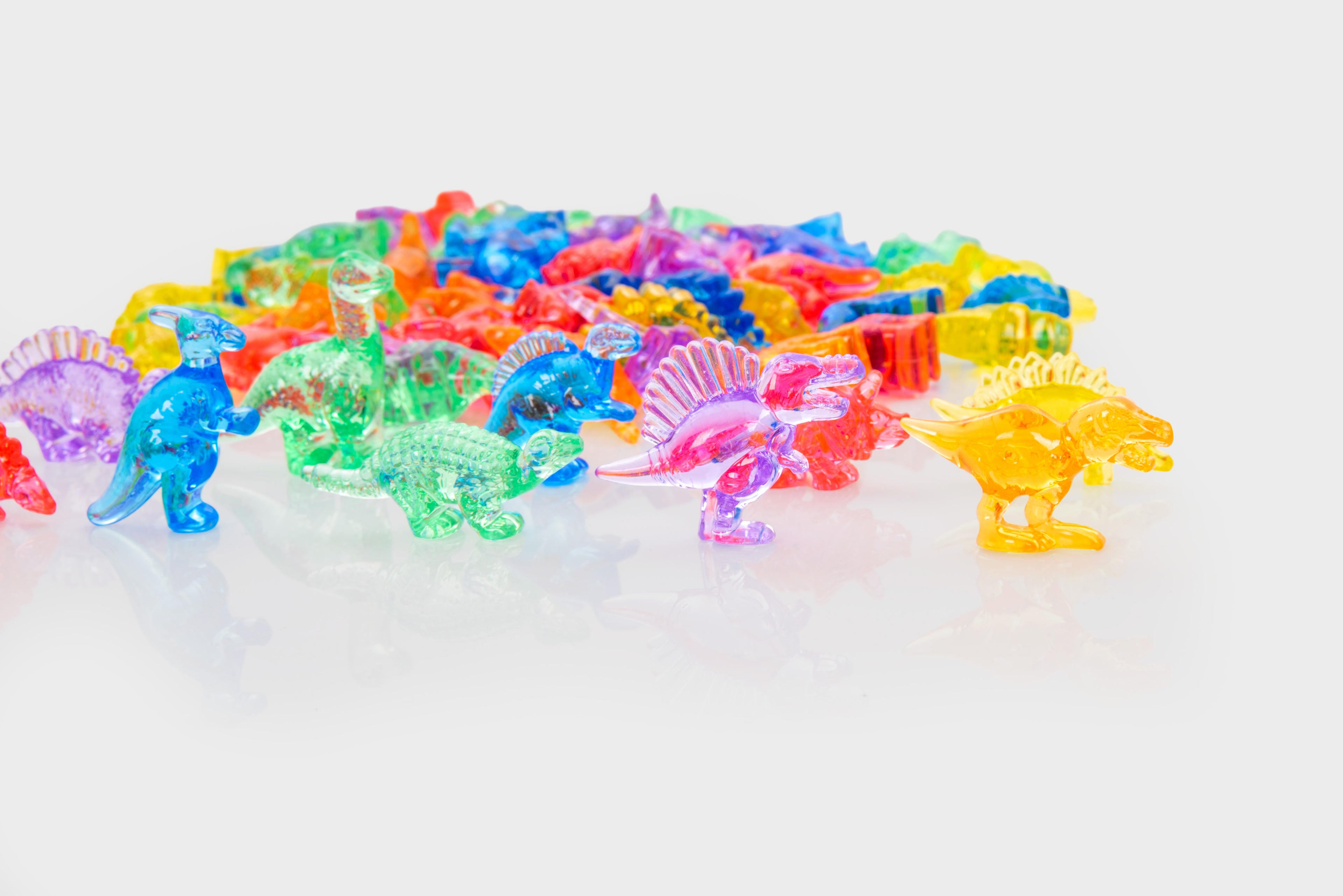 Translucent multicolor dinosaur figurines, arranged in a group on a flat surface.
