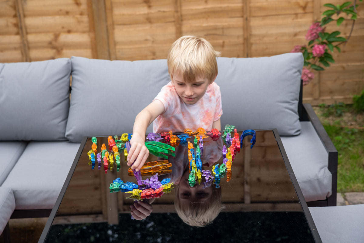 Child playing with translucent multicolor dinosaur figurines on a patio table.