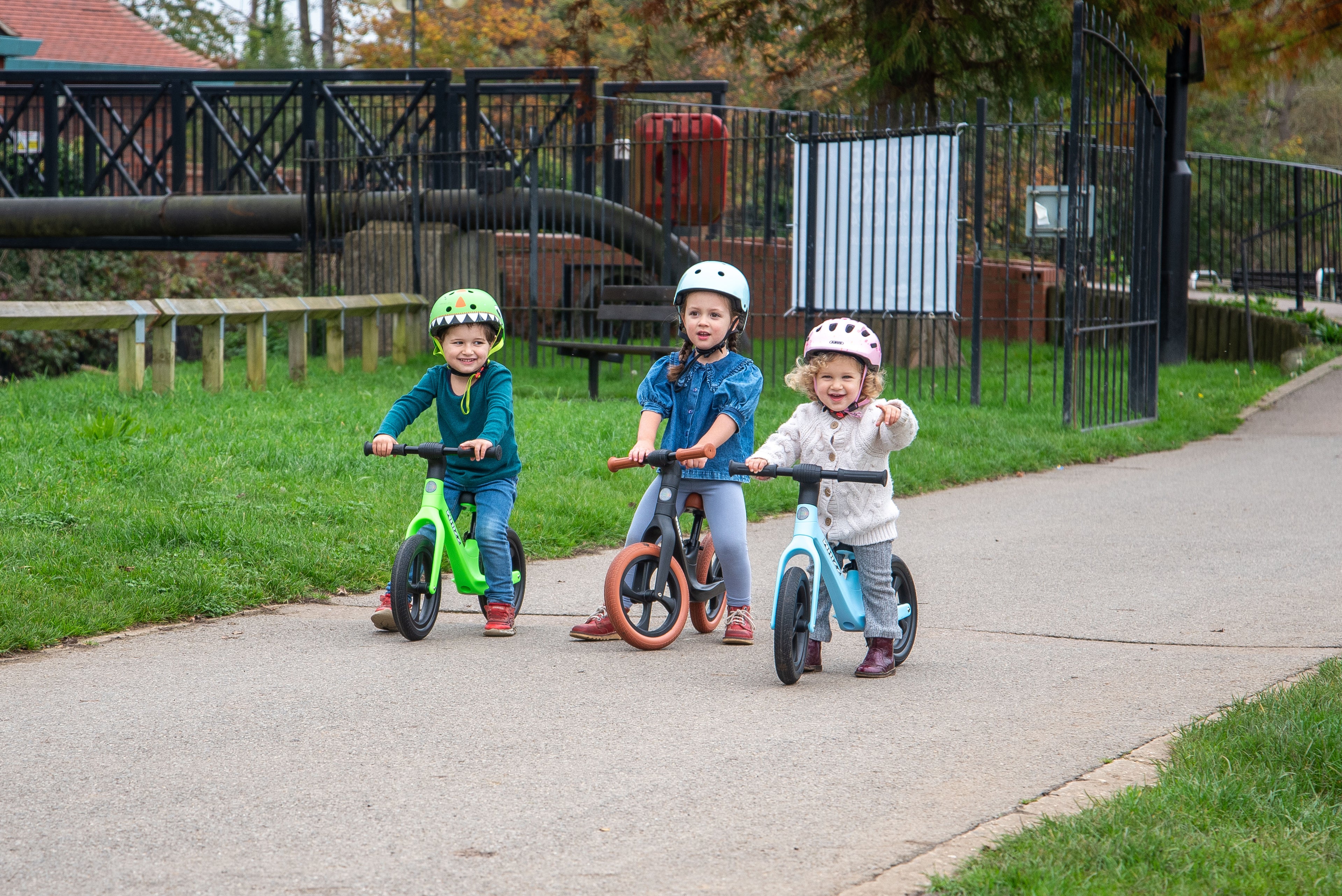 Three kids riding balance bikes in green, orange, and blue with black wheels