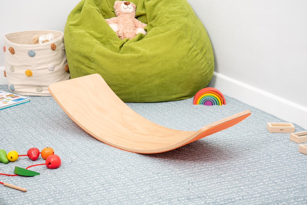 Crescent wooden balance board with orange side, smooth light-wood surface