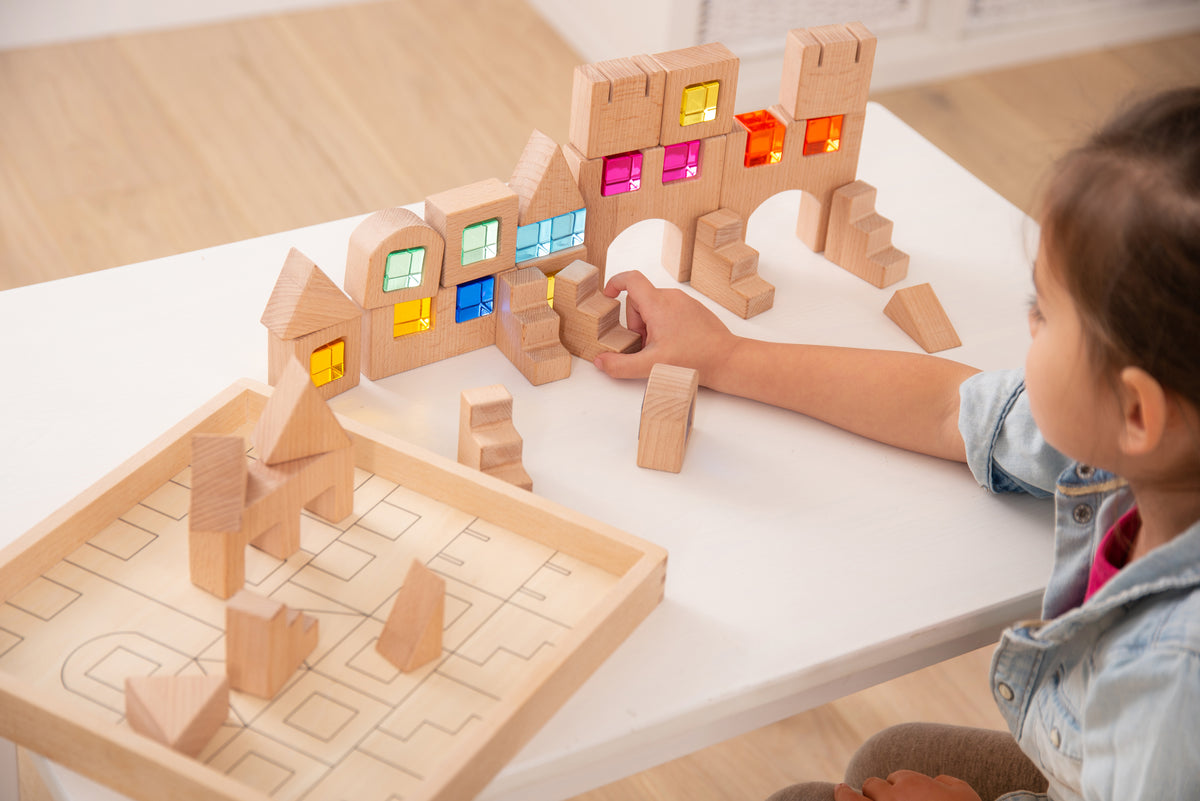 Wooden gem building block set with child arranging blocks near a lit-window house