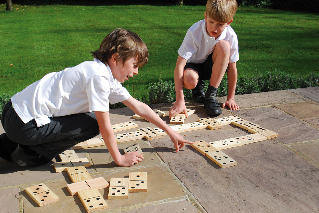 Children arranging wooden domino tiles with black dot pips on a playing grid