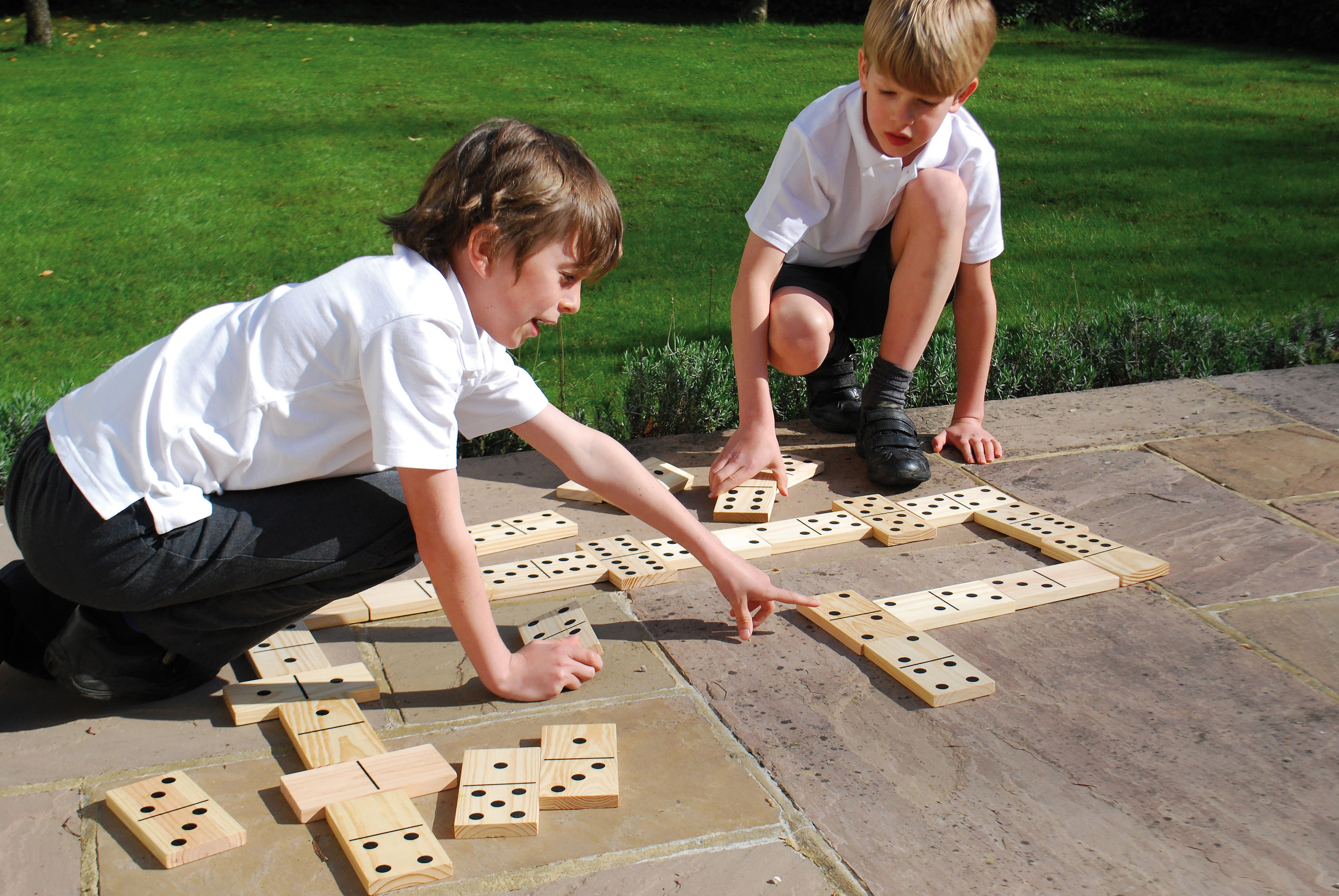 Children arranging wooden domino tiles with black dot pips on a playing grid