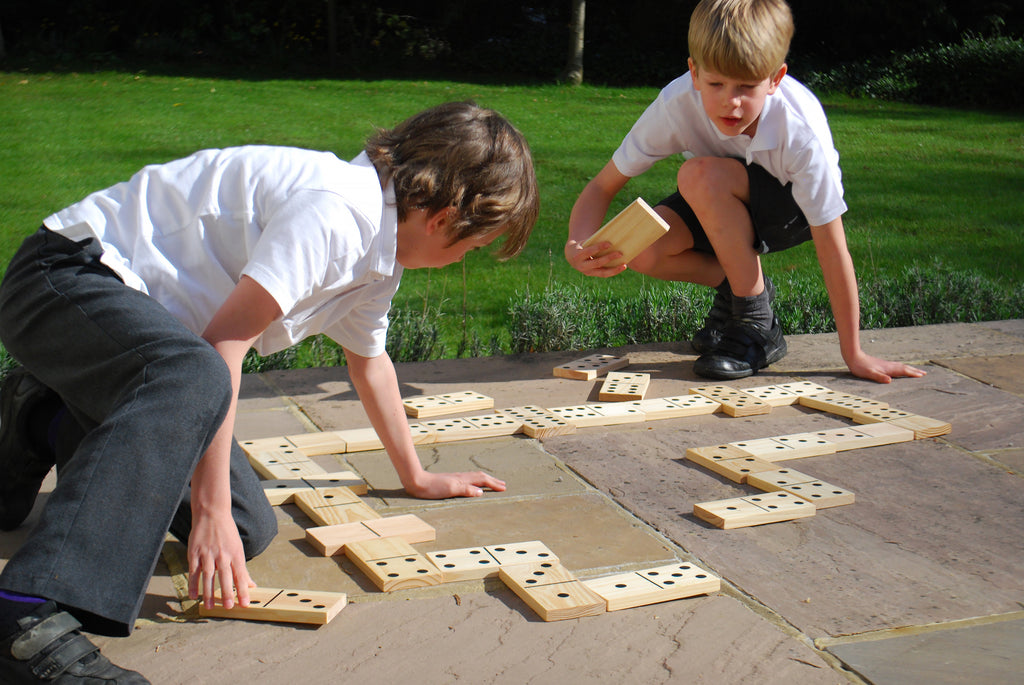 Children kneeling and placing wooden domino tiles with black dot pips