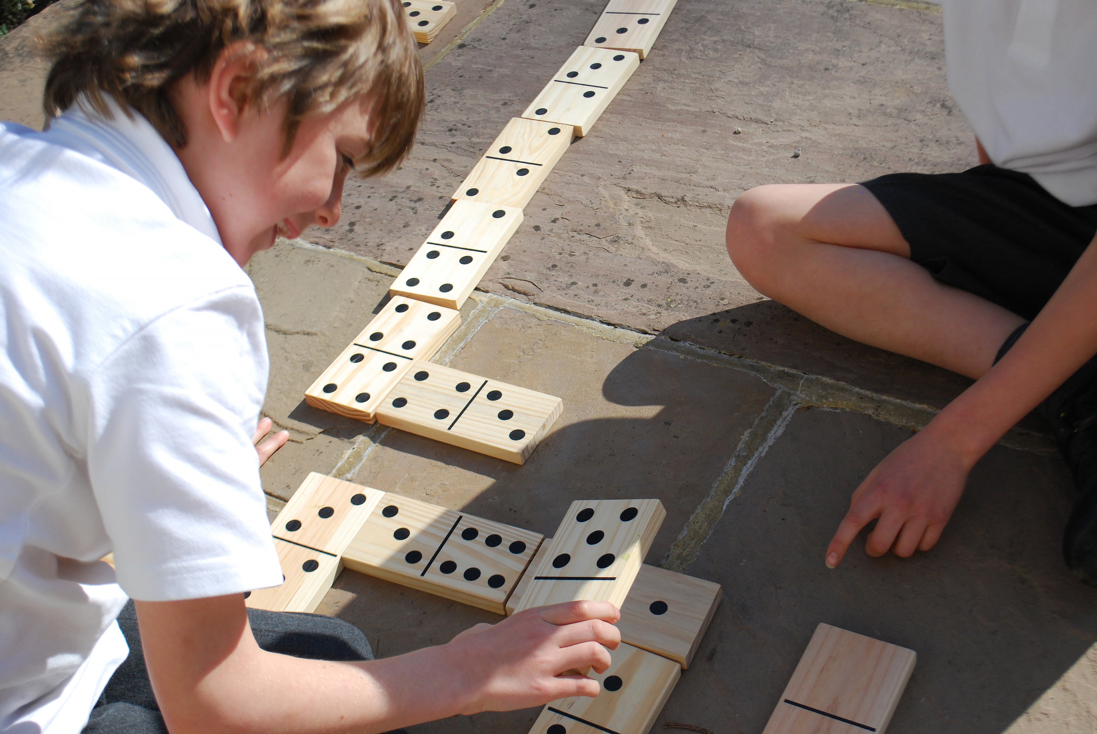 Children placing wooden domino tiles with black dot pips in a long row