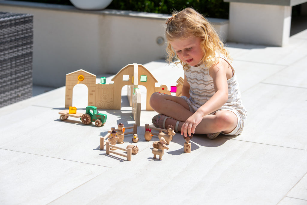 Wooden farm play set with tractor, barn and animal figures on outdoor tiles