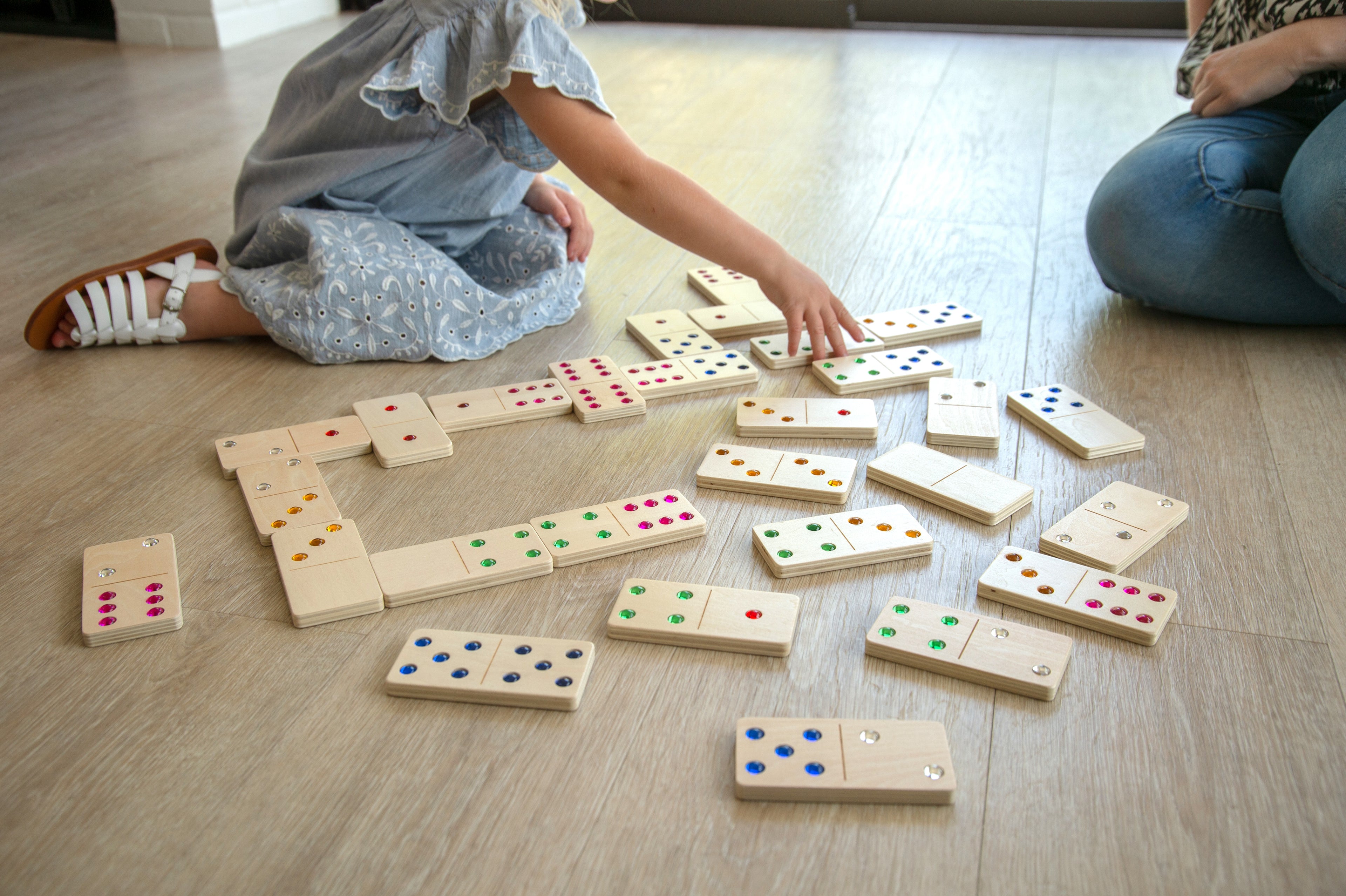 Wooden domino set scattered on the floor, children arranging tiles with colored dots.
