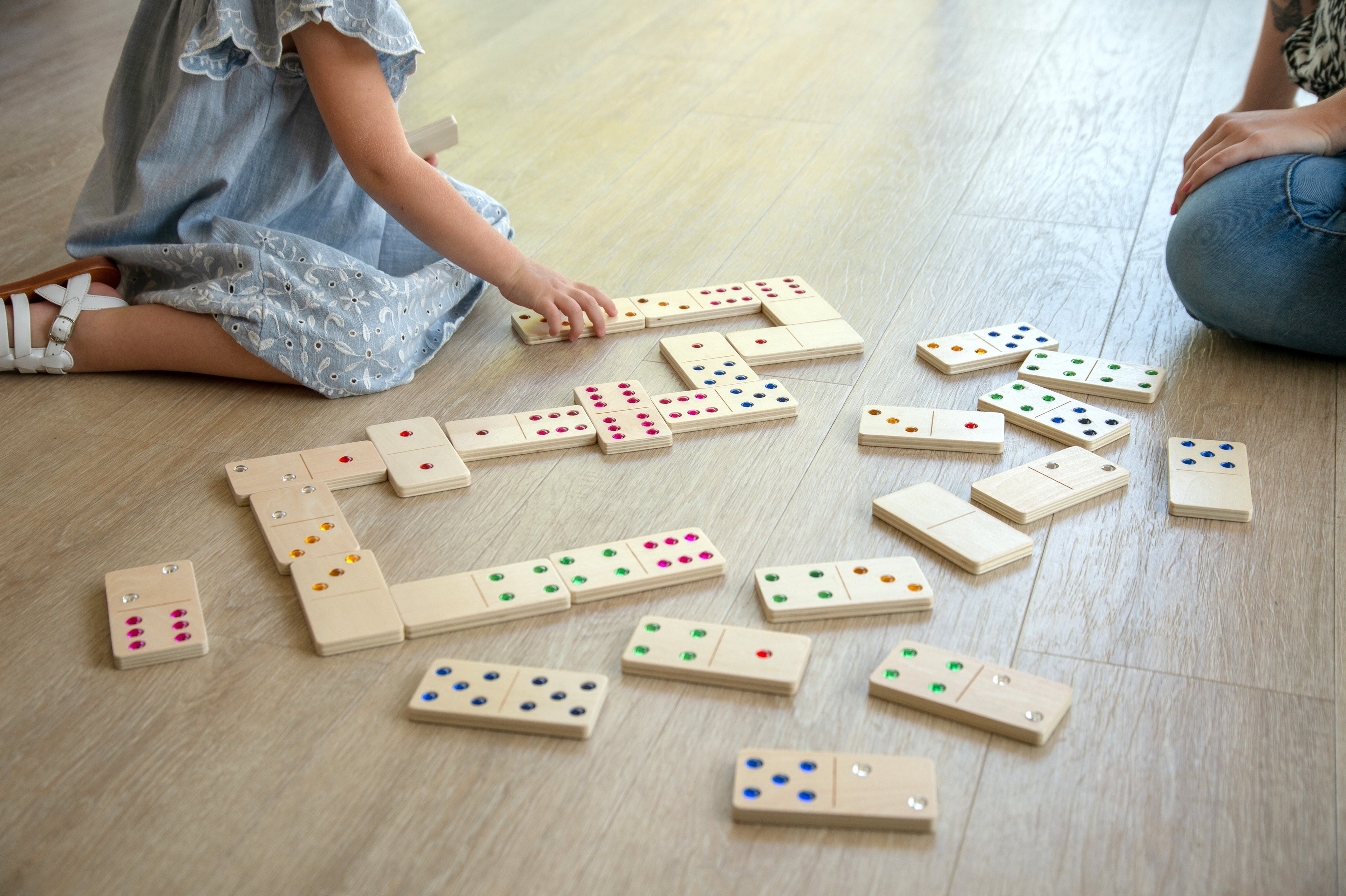 Wooden domino set with colorful dot pips scattered on the floor while kids play.