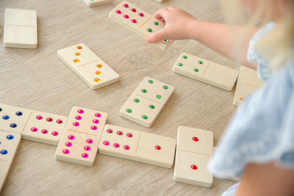 Wooden domino set with colored dot pips on a tabletop, hand arranging tiles.