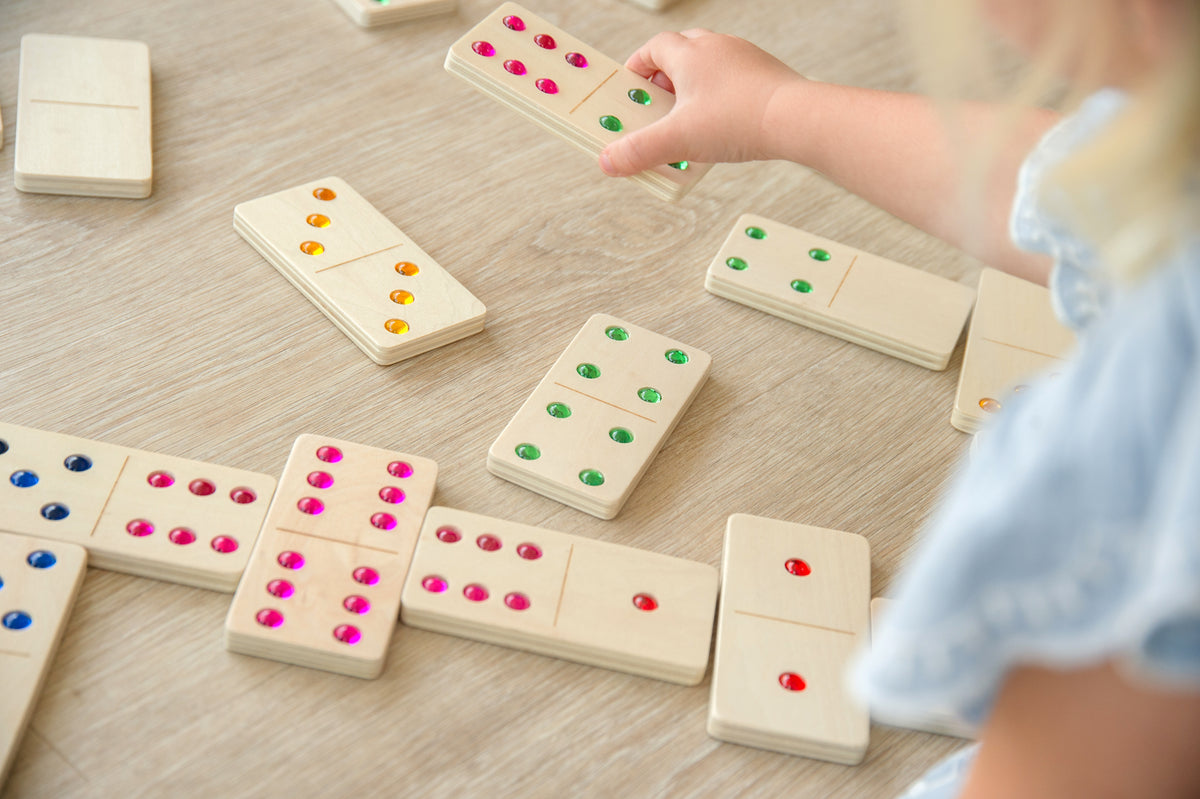 Wooden domino set with colored dot pips on a tabletop, hand arranging tiles.