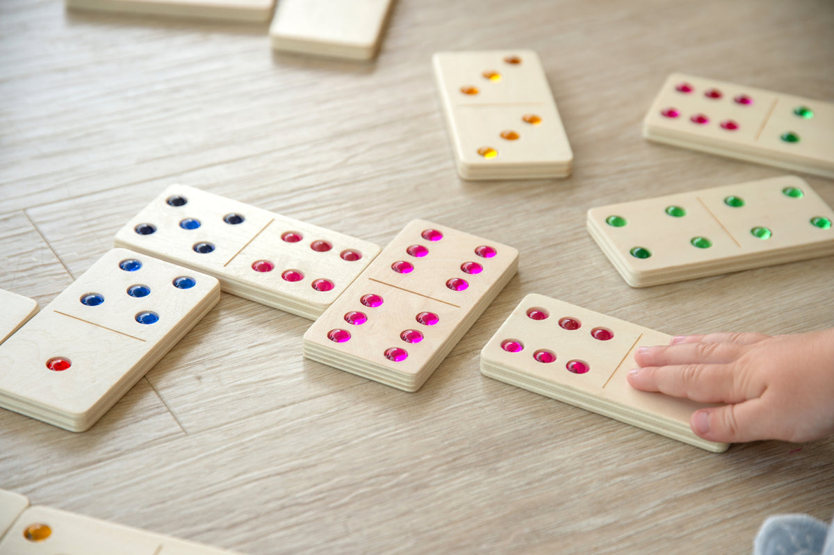 Wooden domino tiles with colored dot pips, hands moving pieces on a table.