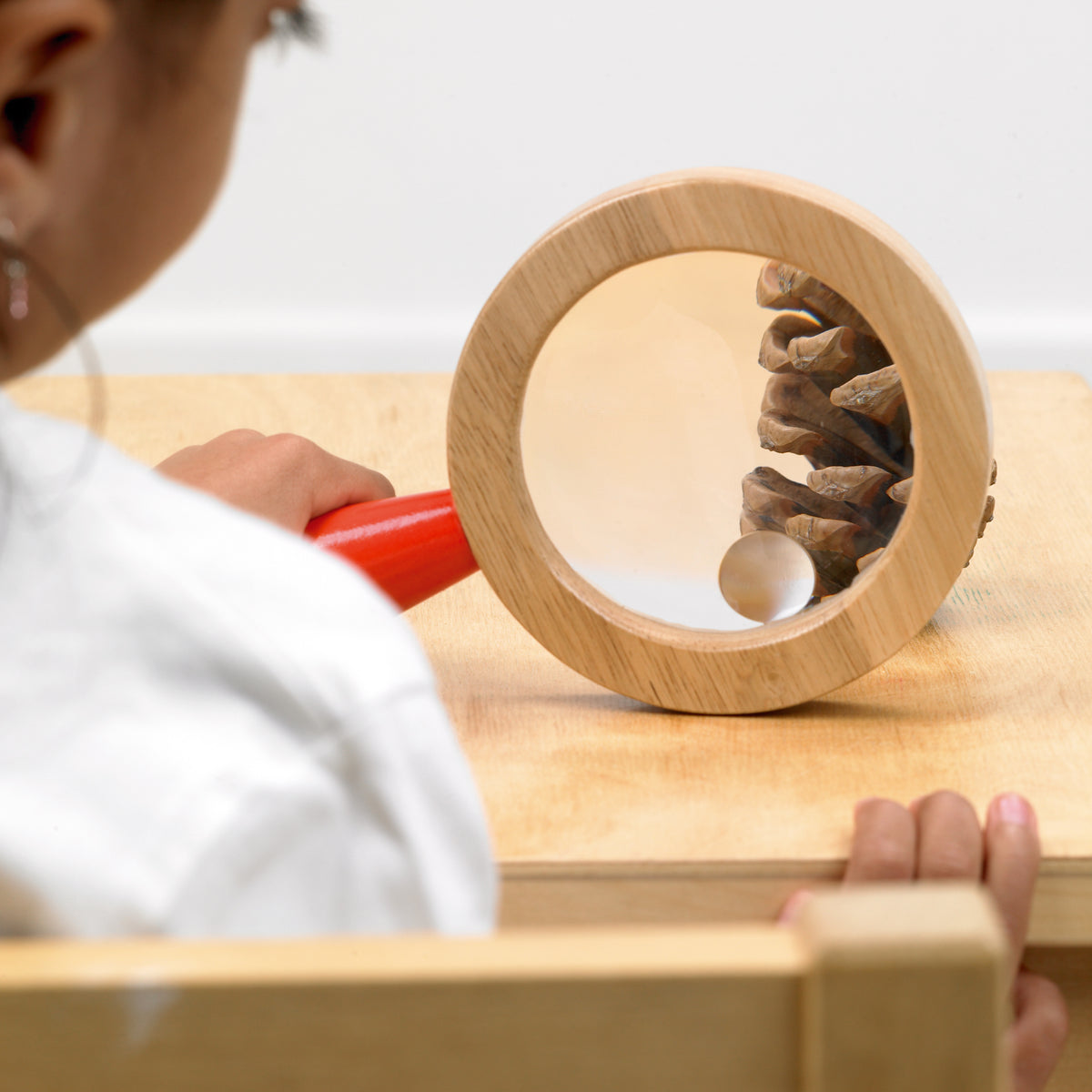 Wooden hand lens on a wooden surface, circular magnifying glass with red handle