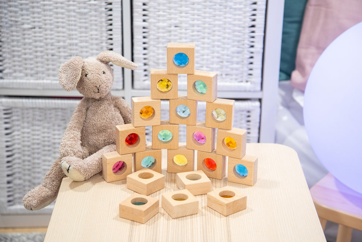 Wooden kaleidoscope blocks pyramid with colorful circular inlays, next to a plush teddy