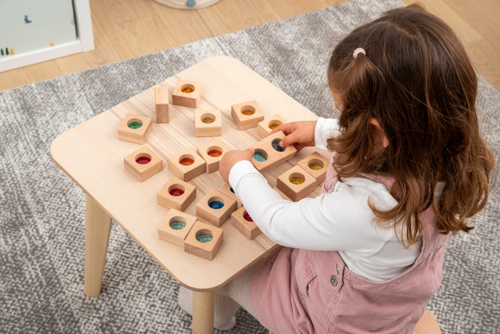 Child arranging wooden kaleidoscope blocks with square cubes and colored circular insets on a table