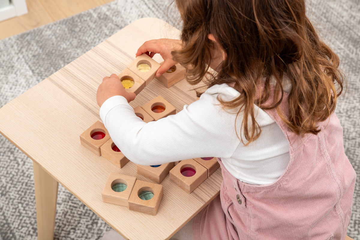 Little girl placing wooden kaleidoscope blocks on a tabletop; square cubes with colored circular inserts
