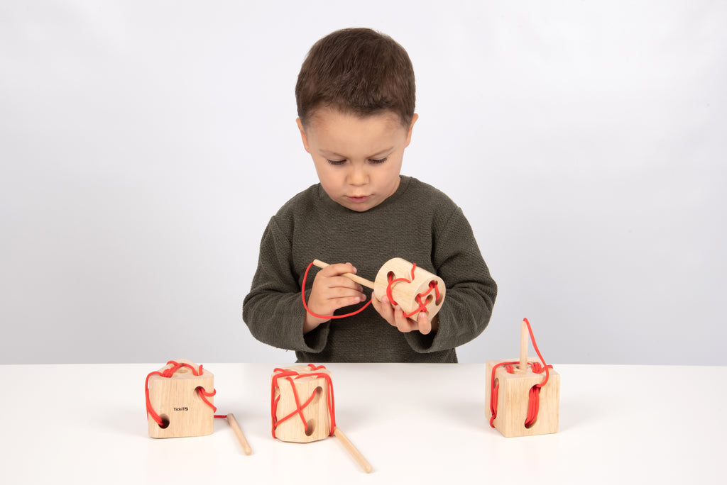 Wooden lacing blocks with red laces and wooden dowel handles, held by child