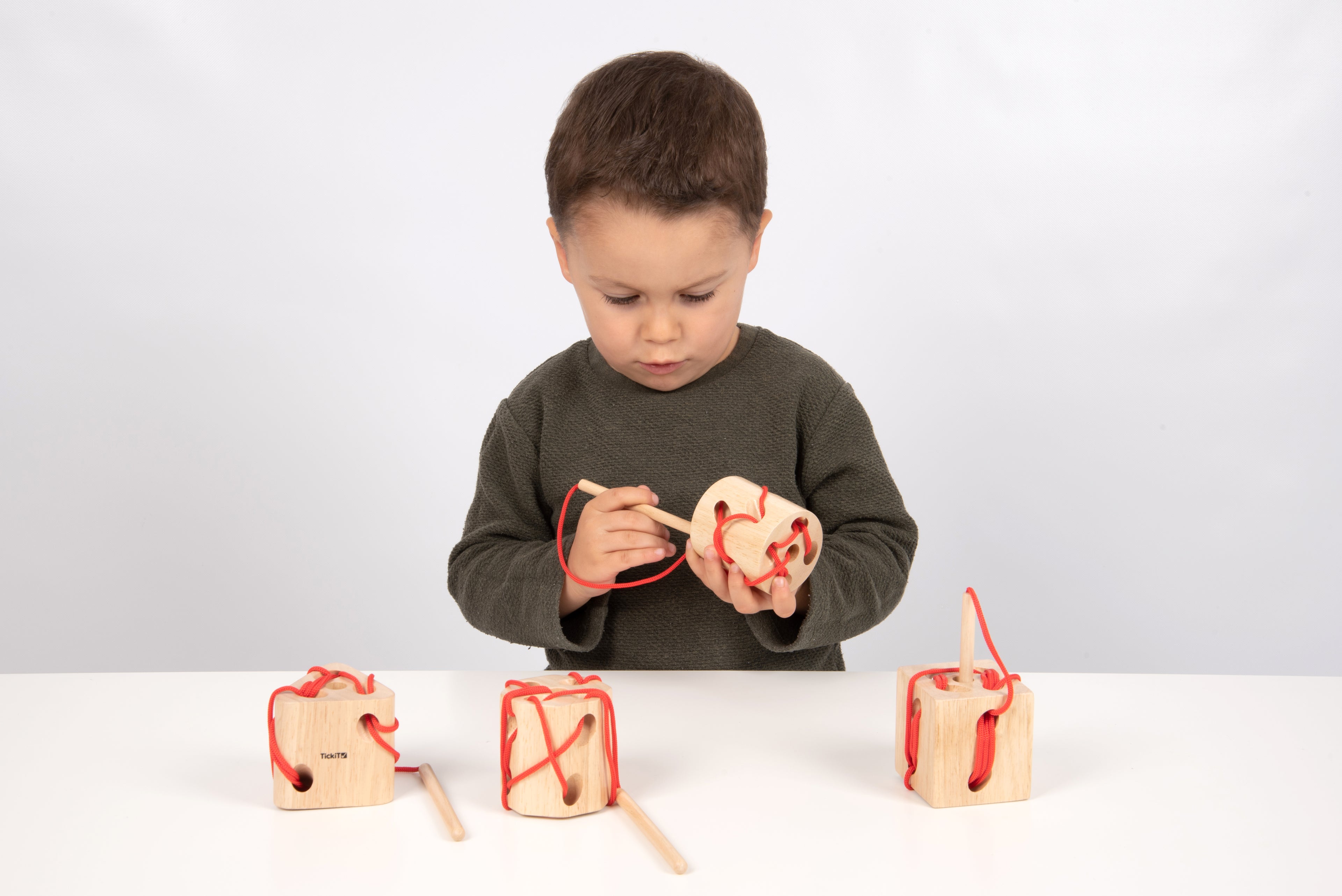 Wooden lacing blocks with red laces and wooden dowel handles, held by child