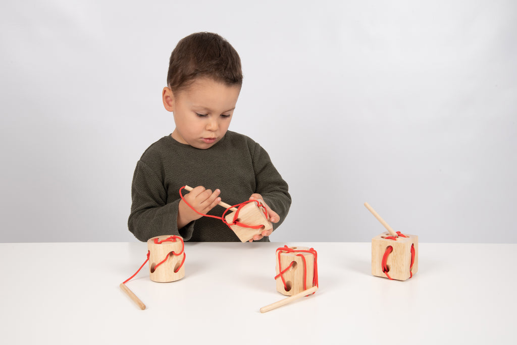 Wooden lacing shape blocks with red laces; child using them on table