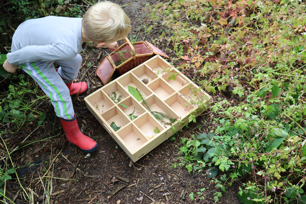Wooden 14-slot sorting tray with dividers, held outdoors with play items